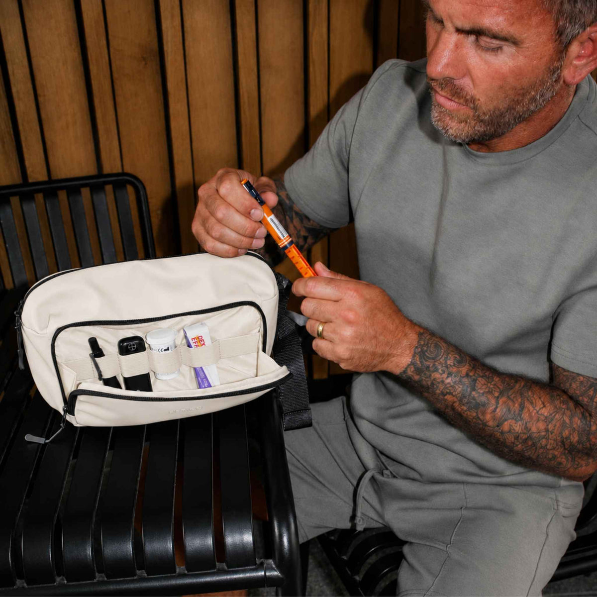 Man seated beside an open cream and black Betico Essential Diabetes Bag, handling an insulin pen with organised diabetes supplies visible in the front compartment.