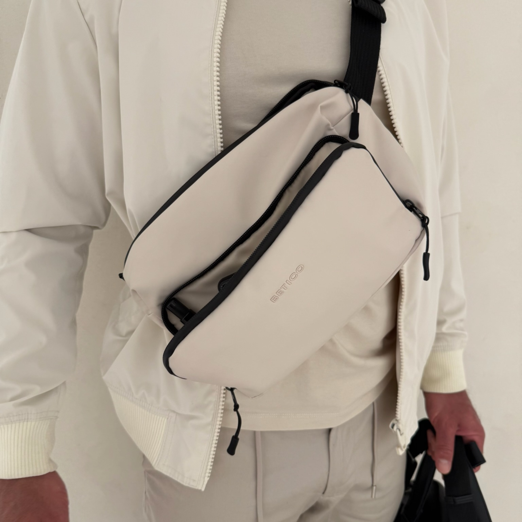Person wearing the cream Betico Essential crossbody organiser bag for discreet everyday travel, organised carry and wellness essentials storage