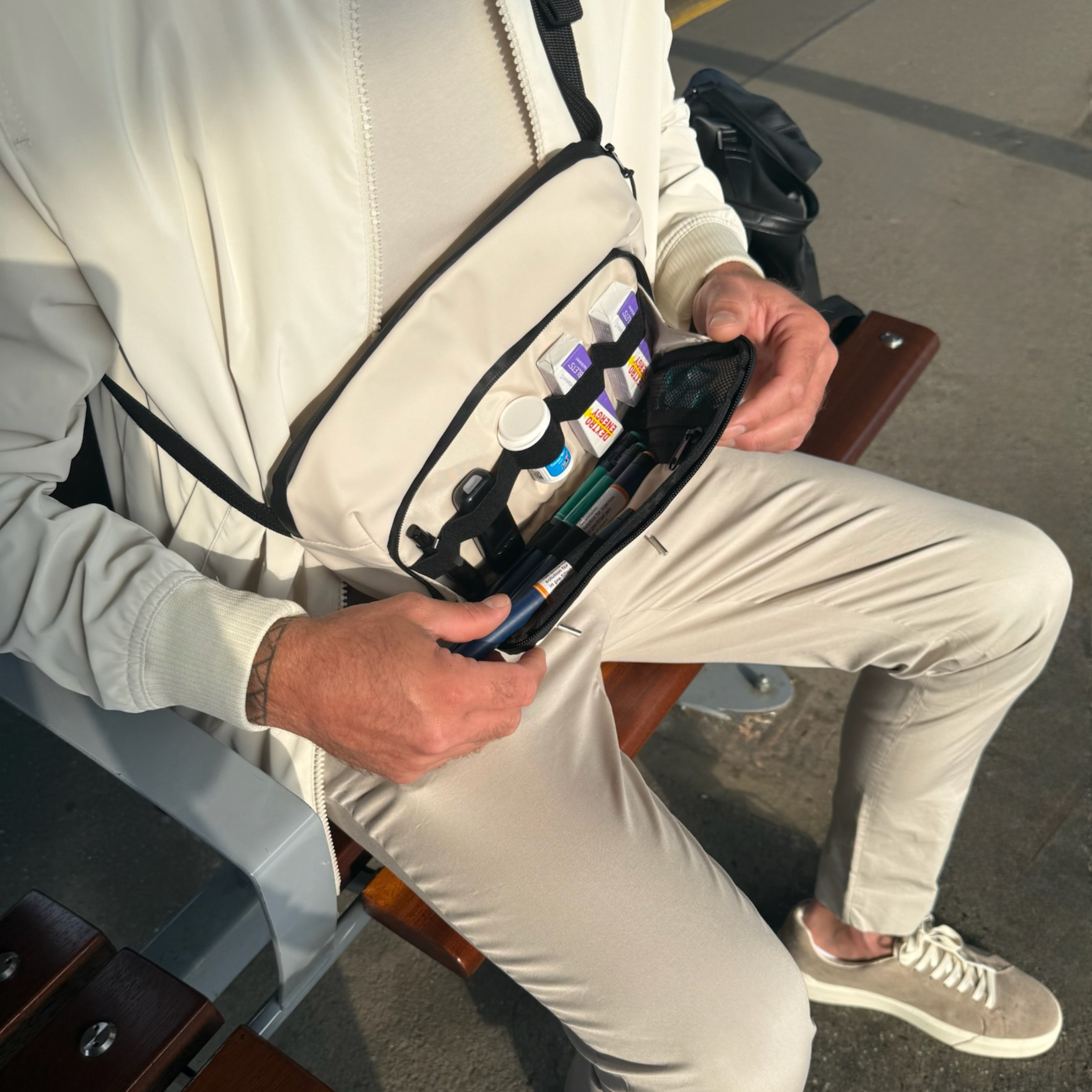 Man using the cream Betico Essential crossbody organiser bag with insulin pens and daily essentials arranged inside for discreet travel and everyday organisation